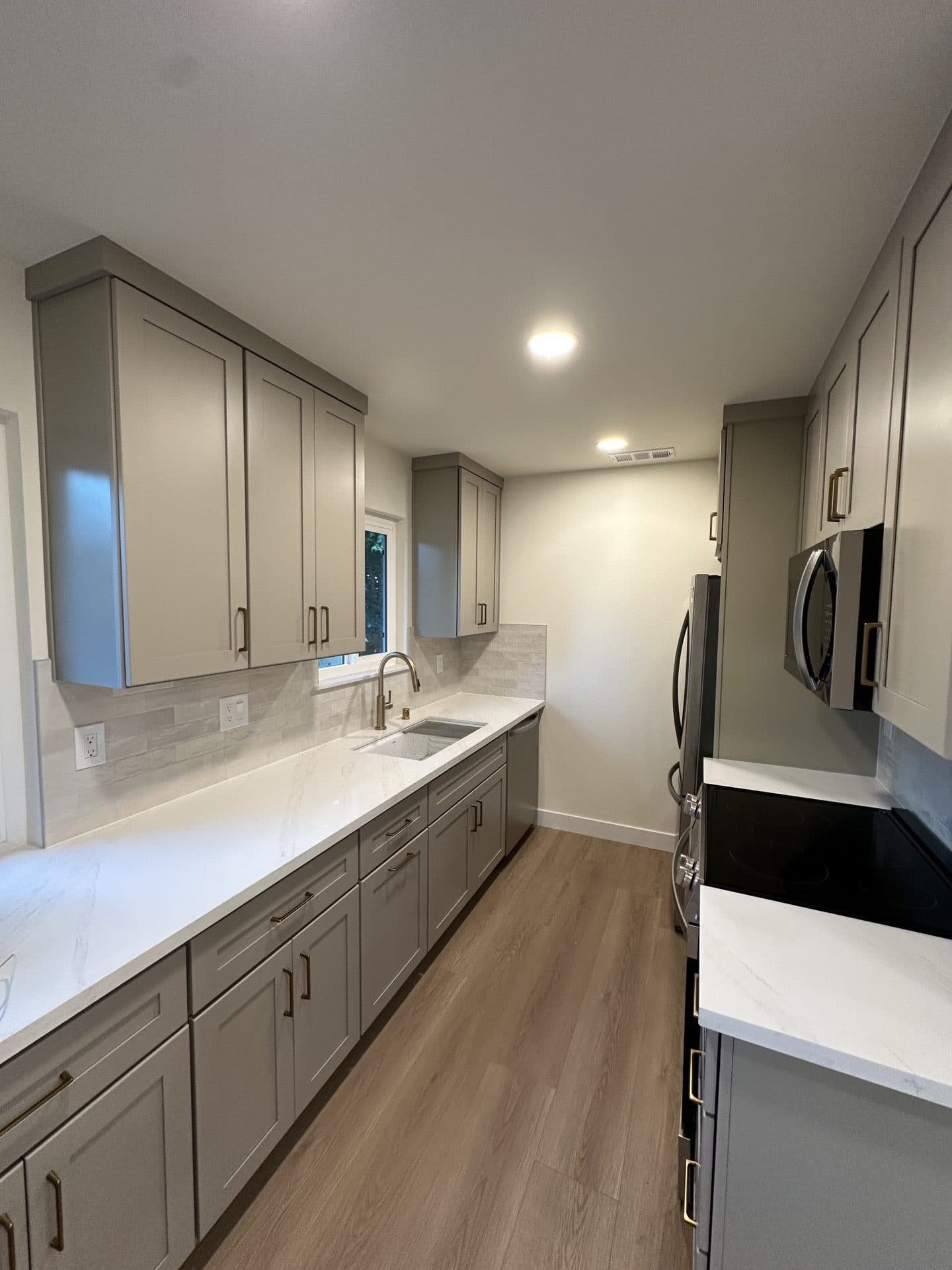Wide-plank natural wood-look flooring running through a finished Fair Oaks kitchen with white cabinets and stone countertops