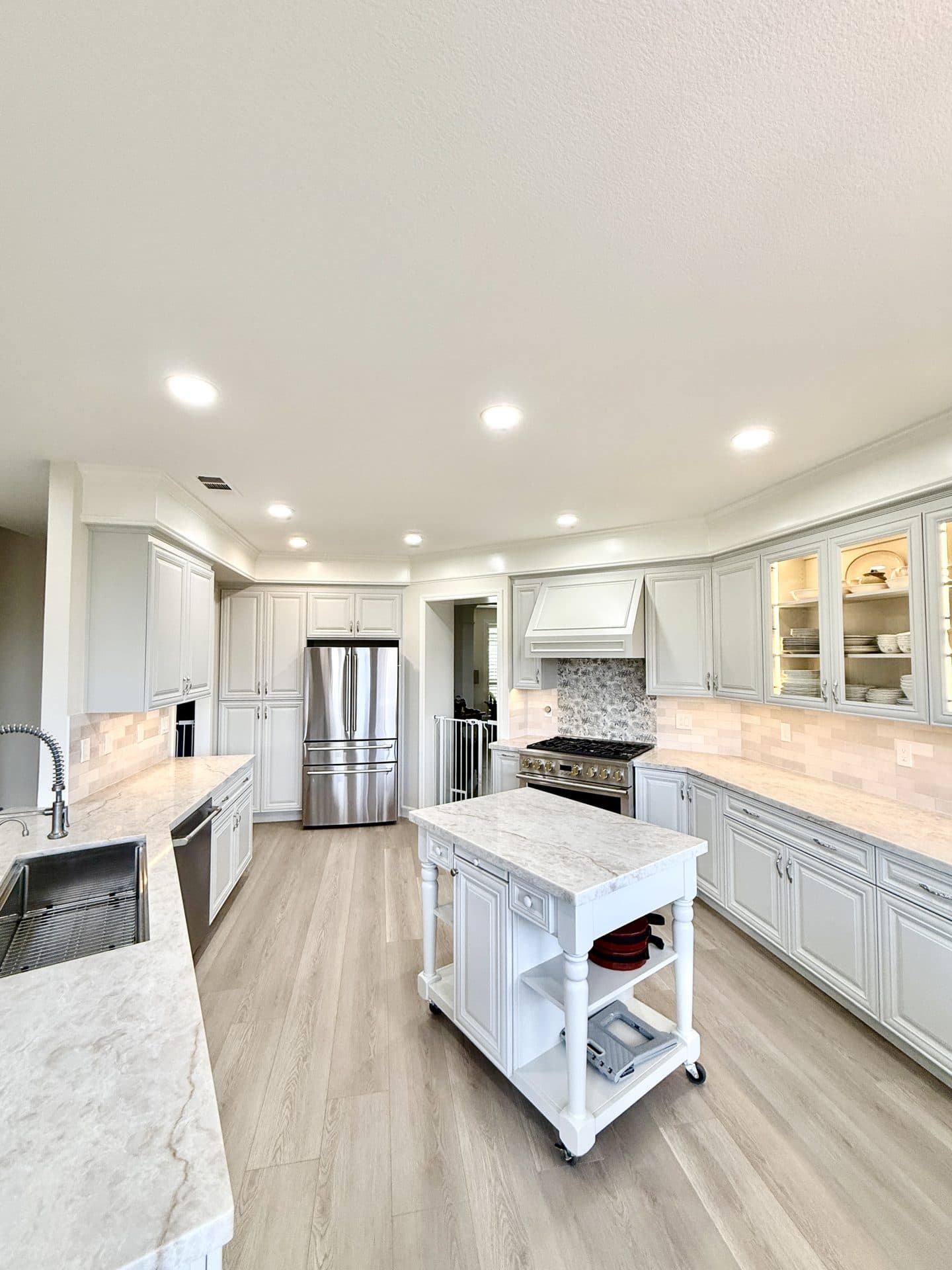 Future Generation Construction Sacramento kitchen remodel — open-plan white kitchen with marble-topped island, custom range hood, glass-front display cabinets and luxury vinyl plank flooring